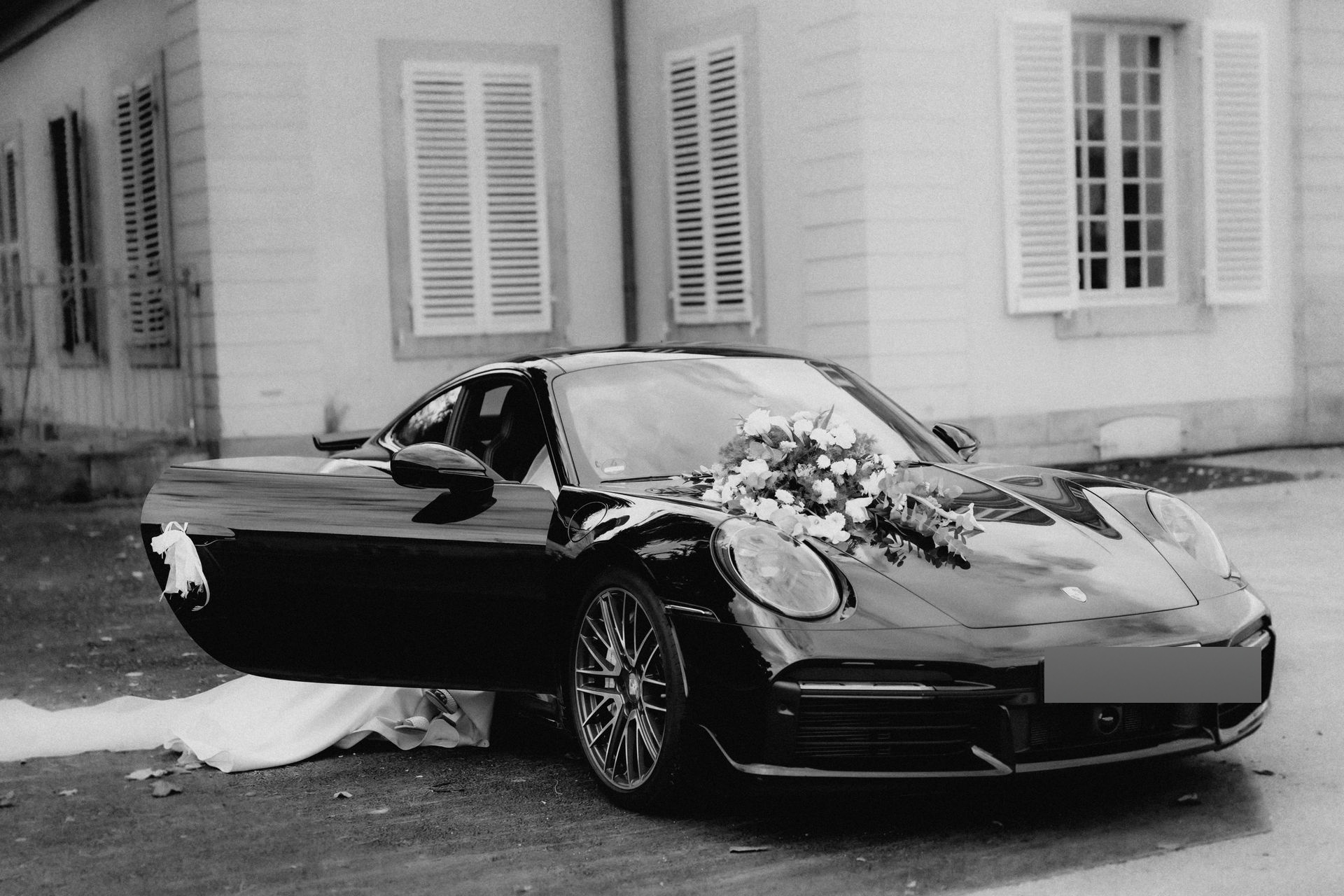 Hochzeitsauto mit Brautstrauß auf der Motorhaube vor Schloss Benrath in Düsseldorf, Schwarzweißaufnahme.