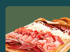 Holzbrett mit verschiedenen Sorten Schinken, Salami und Käse vor grünem Hintergrund.