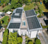 Draufsicht auf ein weißes Haus mit großflächigen Solarmodulen auf dem Dach und einem Garten.