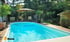 Ein blauer Pool mit Holzdeck in einem grünen Garten, umgeben von Pflanzen und einem Sonnenschirm.