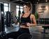 Lächelnde Frau in schwarzer Sportkleidung trainiert an einer Rudermaschine im Fitnessstudio.