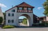 Ein weißes Torhaus mit Fachwerkgiebel und rotem Ziegeldach überspannt eine Straße in einem Dorf.