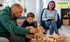 Ein Mann und ein Kind bauen gemeinsam mit Holzklötzen, während eine Frau zuschaut. Logo: KARAWANE Pflegefamilien.