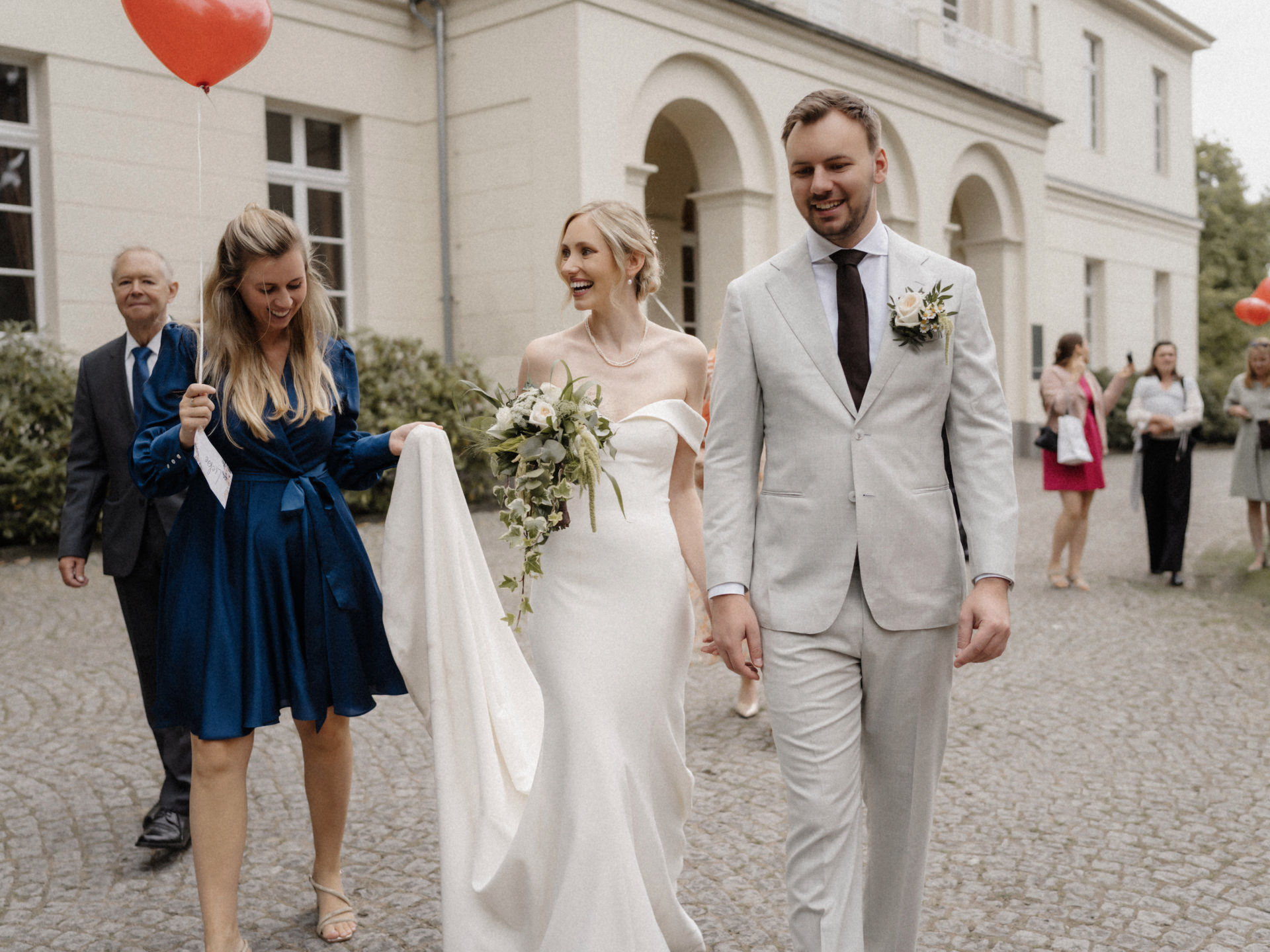 Brautpaar geht vor dem Schloss Eller in Düsseldorf, eine Begleiterin trägt die Schleppe.