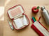 Kleines Notfallset für die Schultasche mit Pflastern, Taschentüchern und Fieberthermometer neben Stiften, Apfel und Trinkflasche
