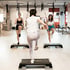 Drei Frauen trainieren auf Steppbrettern in einem Fitnessstudio, die vordere Frau von hinten.