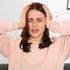 Young woman with brown hair holding her head, eyes closed, showing brain fog and discomfort.