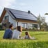 Eine dreiköpfige Familie im Garten vor ihrem Haus mit PV-Anlage