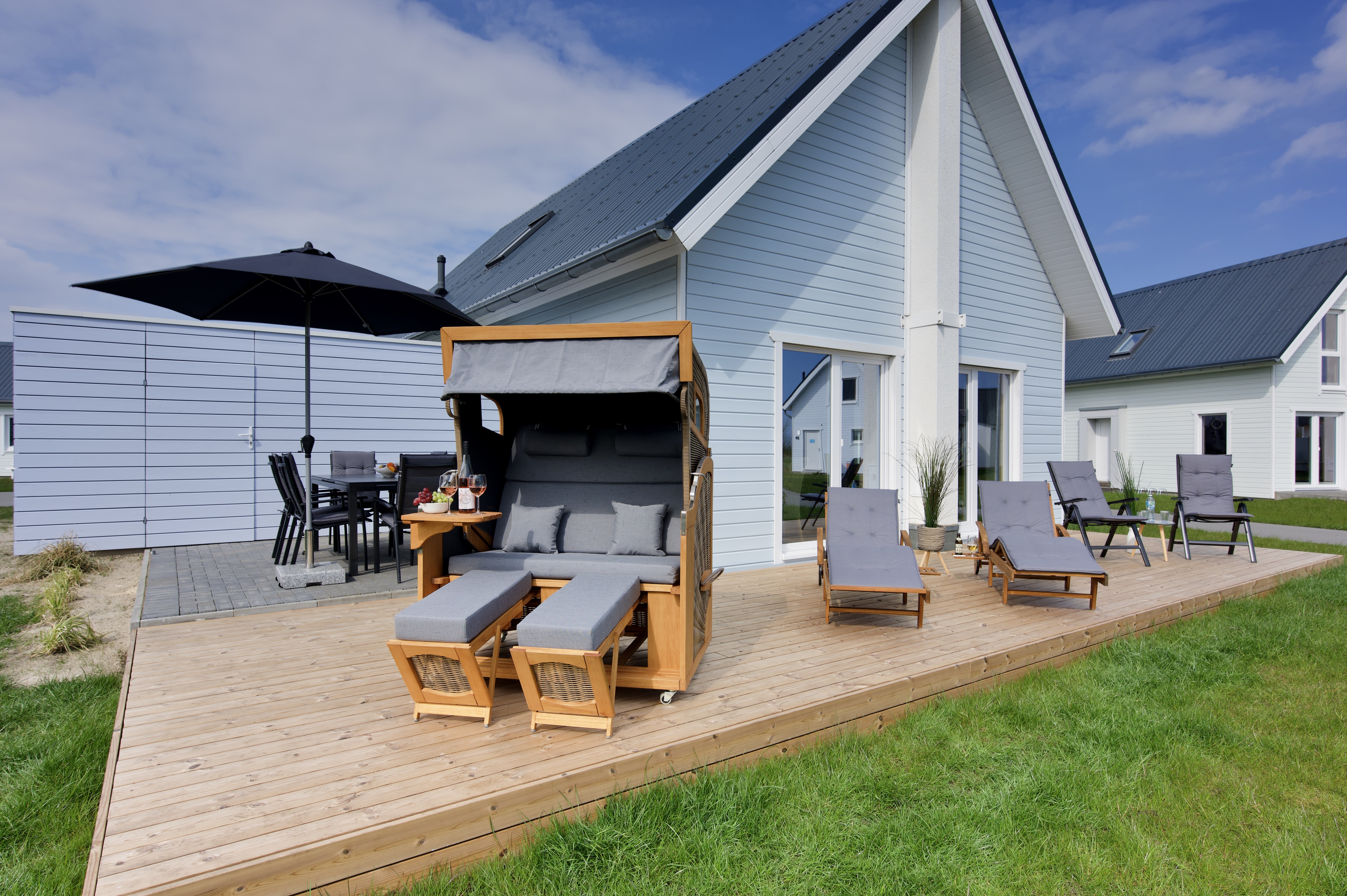 Skipper Galerie im OstseeResort Olpenitz – Holzterrasse mit Strandkorb und Sitzbereich vor einem Ferienhaus