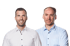 Two men in collared shirts, one smiling, against a dark green background.