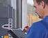 Ein Techniker in blauer Arbeitskleidung bedient mit einem Eingabestift ein Tablet vor einer technischen Steuereinheit.