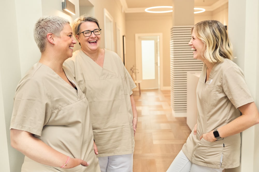 Lachendes Praxisteam in beiger Praxiskleidung