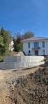 L-Steine aus Beton als Stützmauer für eine Garten-Hangbefestigung vor einem modernen Einfamilienhaus auf einer Baustelle.