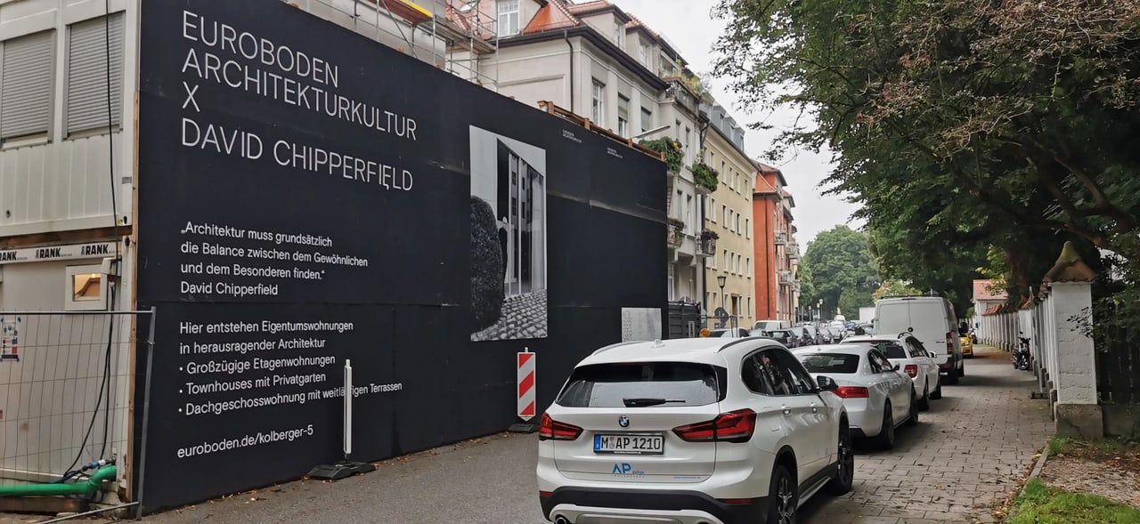 Schwarze Bauwand mit weißer Schrift: EUROBODEN ARCHITEKTURKULTUR X DAVID CHIPPERFIELD, Autos parken daneben.