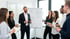 Sechs Kollegen stehen im Kreis und lächeln, ein Mann spricht, ein Flipchart ist im Hintergrund.