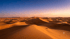 Weite Sanddünen der Sahara bei Sonnenuntergang unter einem violett-blauen Himmel.