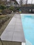 Große graue Terrassenplatten werden am Rand eines hellblauen Swimmingpools auf einer Baustelle im Garten verlegt.