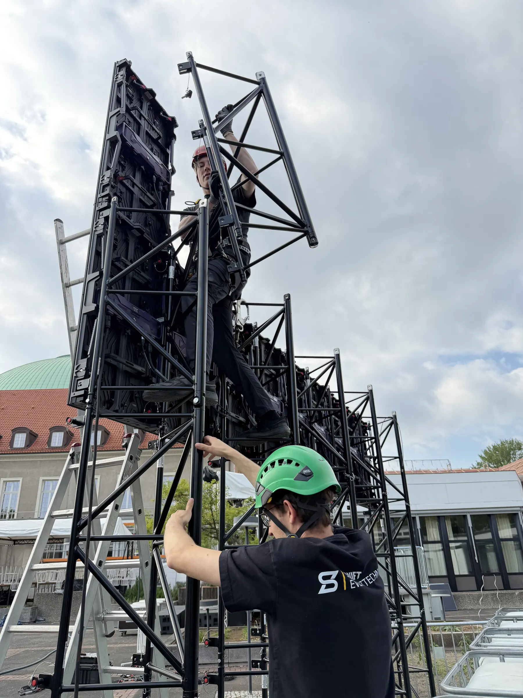 Techniker mit Helm klettert am Tri-Frame-System hinter der LED-Wand