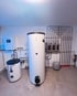 Zwei weiße Warmwasserspeicher und ein Wandverteiler mit Rohren sind in einem Heizungsraum installiert Reutte