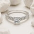 Verlobungsring aus Weißgold mit einem zentralen Brillanten und diamantbesetzter Ringschiene zwischen weißen Steinen.