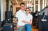 Ein lächelnder Mann und eine Frau in weißen Poloshirts stehen Arm in Arm in einem modernen Fitnessstudio mit Trainingsgeräten.