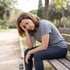 A woman in athletic wear sits on a park bench with her head in her hand, appearing tired or stressed after a workout.