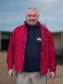 Porträt von Zbignév Jacek, Vorarbeiter/Teamleiter bei Zenith Umzüge, in roter Jacke vor blauem Hintergrund