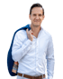 Ein Mann mit weißem Hemd und blauem Blazer über der Schulter lächelt leicht in die Kamera.