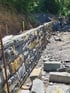 Eine im Bau befindliche Natursteinmauer aus grauen und gelblichen Quadersteinen an einem Hang.