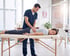 A healthcare provider in blue scrubs performs a manual adjustment on a woman's lower back on a treatment table.