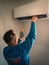 Techniker in blauem Hemd prüft Bosch Klimaanlage mit orange-blauem Messgerät.