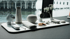 Minimalistisch arrangierter Tisch mit Smart Speaker, Thermosflasche, Kamera, Blumenvase und technischen Accessoires vor großem Fenster mit Blick auf Wasser und Gebäude – stilvolle Kombination aus Technologie, Design und moderner Wohnästhetik.