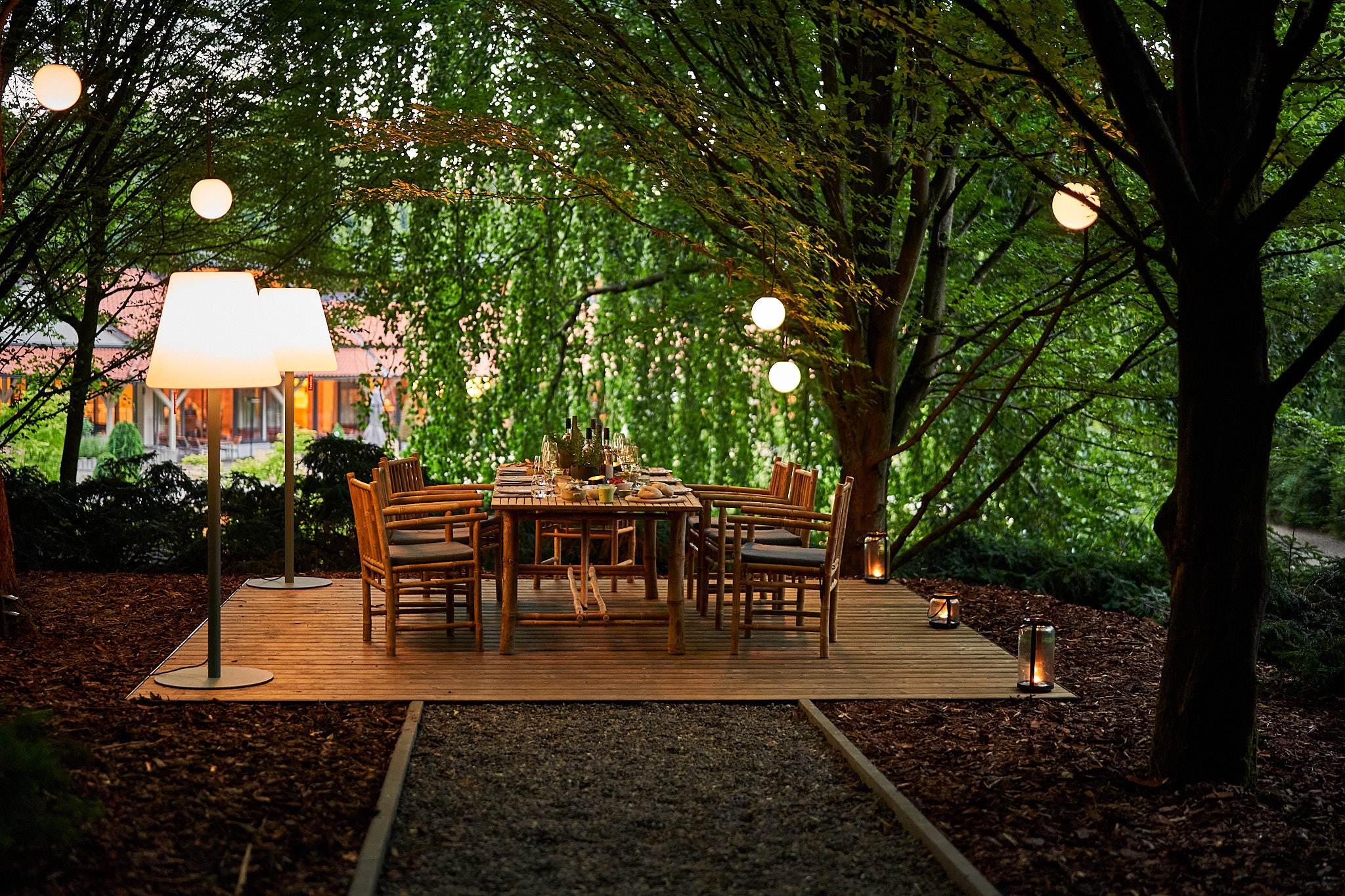 Waldhotel FREIgeist Northeim – Holzterrasse mit Esstisch und Beleuchtung unter Bäumen