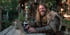 Man with long hair and beard in fur-trimmed clothing smiling while typing on a laptop outdoors.