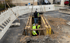 Zwei Bauarbeiter in Warnwesten arbeiten in einem offenen Graben mit Spundwänden auf einer Baustelle.