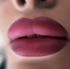 Nahaufnahme von vollen Lippen, die mit mattem, dunklem Rosa oder Beerenlippenstift geschminkt sind.