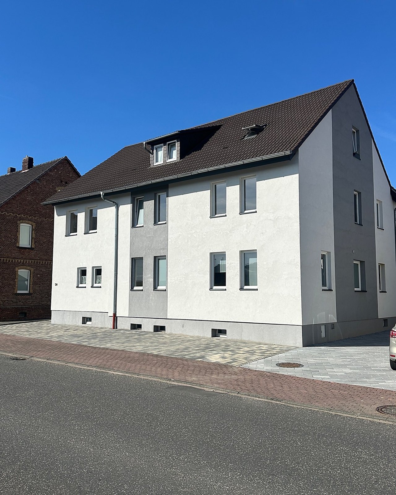 Außenansicht eines modernisierten Mehrfamilienhauses mit heller Fassade und Satteldach.