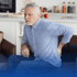 An older man in a kitchen, holding his back.