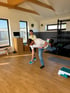 Ein Mann führt eine Standwaage-Übung in einem hellen Fitnessstudio unter Anleitung einer Trainerin aus.