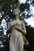 Statue einer Frau aus Stein, die mit den Händen auf der Brust zum Himmel blickt.