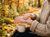 Hände im Strickpullover cremen sich draußen im Herbstlicht ein