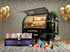 Schwarzer Cocktailbar-Truck mit offener Klappe, davor ein Getränkespender, bunte Cocktails und goldene Ballons.