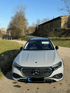 Grauer Mercedes Benz E-Klasse Kombi steht auf einem Feldweg mit Bäumen und Scheune im Hintergrund.