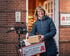 Eine lächelnde Frau in Winterjacke hält ein Paket neben ihrem Fahrrad mit einem Korb der Insel-Apotheke.