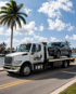 Towing Port Charlotte flatbed tow truck transporting an SUV along a waterfront road with palm trees.