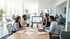 Vier Personen am Besprechungstisch, eine Frau zeigt auf ein Diagramm auf einem Monitor, andere Mitarbeiter im Hintergrund.