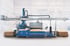 Blaue und graue Holzverarbeitungsmaschine mit Holzstapeln in einer Fabrikhalle.