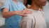 Chiropractic care professional in blue scrubs gently massages a patient's shoulders.