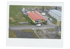 Luftaufnahme eines gelben Gebäudes mit rotem Dach, umgeben von grünen Wiesen und einem grauen Parkplatz.