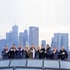 Zehn Personen stehen auf einem Dach mit Blick auf die Frankfurter Skyline, zeigen mit dem Daumen nach oben.